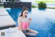 A woman in a pink bikini sitting by a swimming pool.