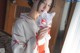 A woman in a kimono holding a white cat mask.