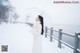 A woman in a white coat holding an umbrella in the snow.