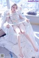 A woman sitting on top of a bed covered in white sheets.